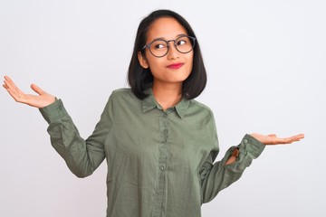 Young chinese woman wearing green shirt and glasses over isolated white background clueless and...