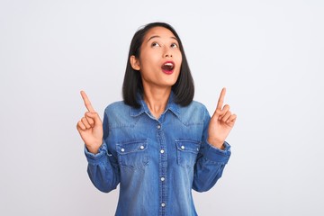 Young beautiful chinese woman wearing denim shirt standing over isolated white background amazed...