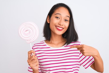 Young beautiful chinese woman eating lollipop standing over isolated white background with surprise face pointing finger to himself
