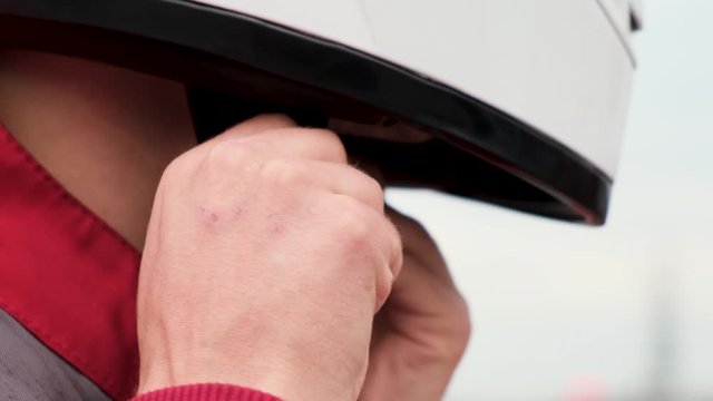 Extreme close up of a man trying to take off white protective helmet on bright sky background. Media. Young man is trying to unfasten his safety helmet to take it off.