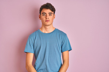 Teenager boy wearing casual t-shirt standing over blue isolated background with serious expression...