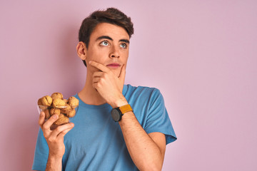 Teenager boy holding bunch of natural walnuts over pink isolated background serious face thinking about question, very confused idea