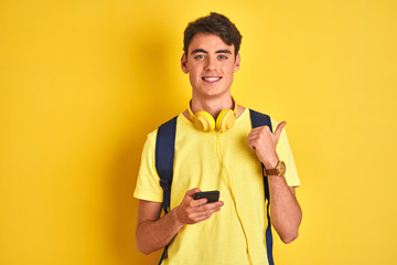 Teenager boy wearing headphones and using smartphone over isolated background pointing and showing...