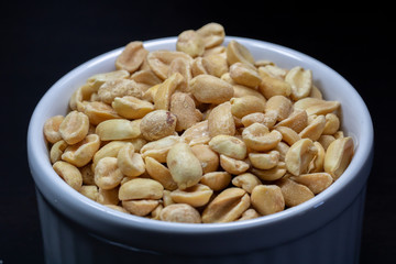 macro photography of shelled and salted peanuts in a white canister with black background