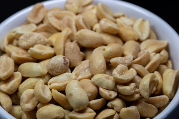 macro photography of shelled and salted peanuts in a white canister with black background