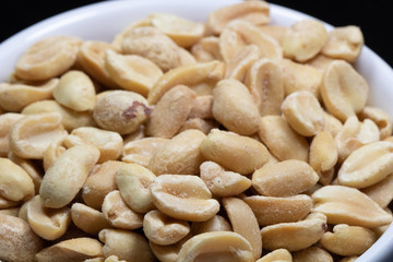 macro photography of shelled and salted peanuts in a white canister with black background