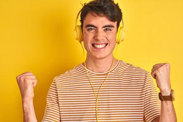 Teenager boy wearing headphones over isolated yellow background celebrating surprised and amazed for success with arms raised and open eyes. Winner concept.