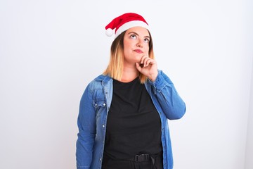 Young beautiful woman wearing Christmas Santa hat standing over isolated white background with hand on chin thinking about question, pensive expression. Smiling with thoughtful face. Doubt concept.