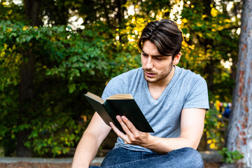 Young man reads a self-absorbed novel sitting in a park at sunset, enjoying ancient literature.