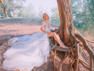 A mysterious, slender blond woman in a luxurious white dress. snow queen, sits near a tree with...