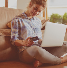 Beautiful young woman using credit card and laptop for online shopping