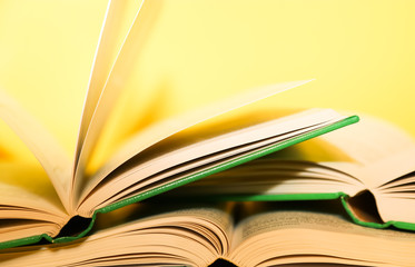 Yellow book stack, book pages turning, over a yellow background. 