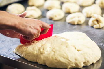 pastry chef cuts piece of dough with plastic spatula and forms buns.