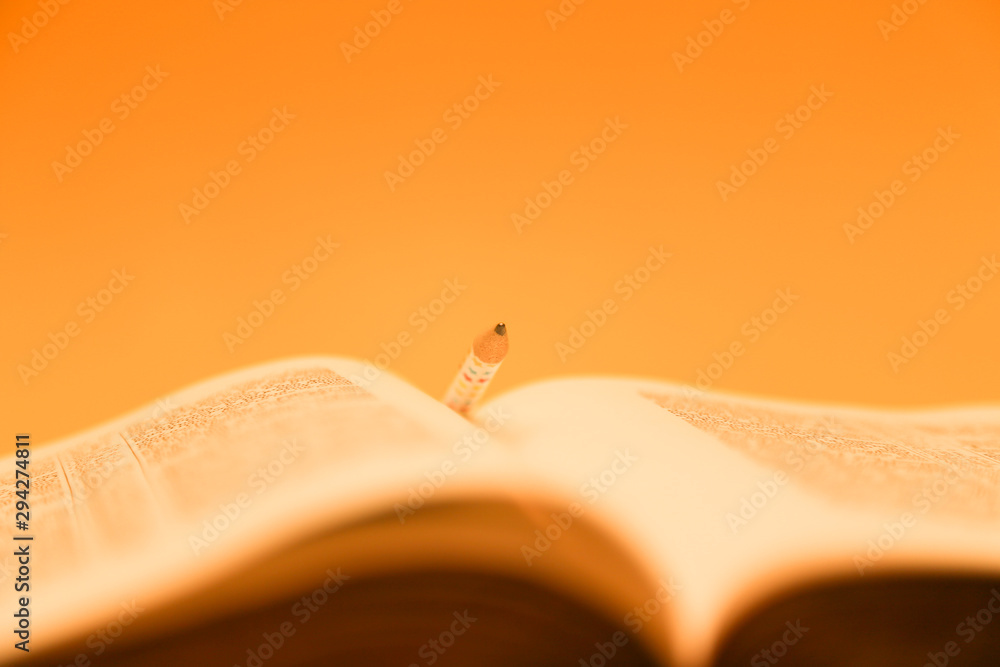 Wall mural bible with a pencil in the pages. gold coloured crop of bible, over yellow - Wall murals