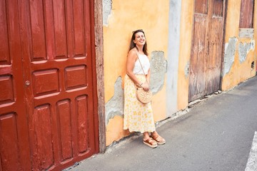 Fototapeta premium Beautiful girl leaning on orange wall, young friendly woman smiling happy on a sunny day of summer