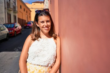 Fototapeta premium Beautiful girl leaning on orange wall, young friendly woman smiling happy on a sunny day of summer