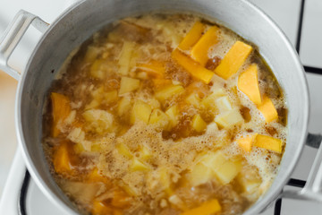 Pumpkin soup cooking in sausepan in the kitchen on the stove. Autumn traditional food