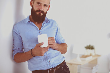 Full length of young businessman having coffee while leaning on sliding door