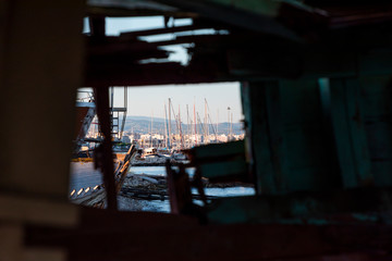 Sail boats as seen through a hole in an old wooden fishing boat on dry dock.