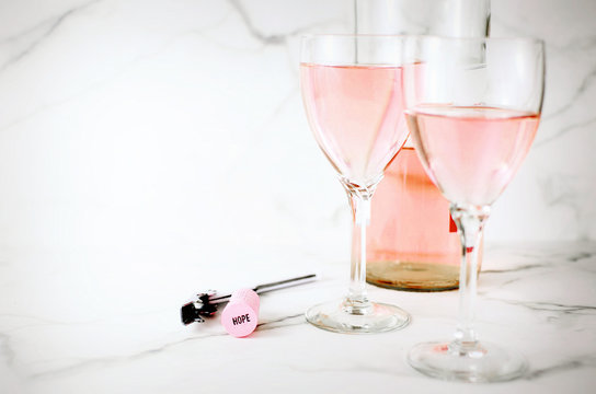 Hi key image for breast cancer awareness month in October includes rose winw on  marble table.Two glasses of wine and a corkscrew with a pink cork and the word hope is stamped on the cork. Copy space