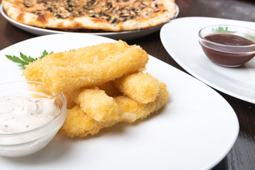 Cheese sticks breaded, with sauce and herbs, on a platter.