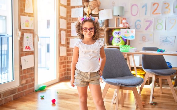 Beautiful toddler wearing glasses and unicorn diadem standing and smiling at kindergarten