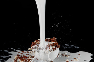 white bowl with assorted cereal with powerful milk stream isolated on black