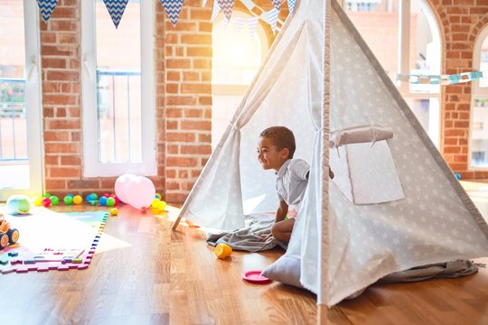 Beautiful african american toddler playing inside tipi smiling at kindergarten