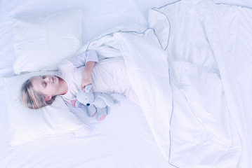 Child little girl sleeps in the bed with a toy teddy bear.