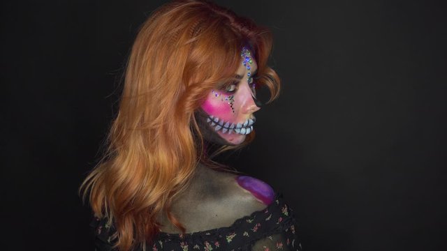 voodoo magic, mysterious girl with bright red orange hair stands back and turns to face camera, sweet sugar pink skull and black dress with bare shoulders, creative Halloween image of art makeup
