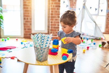 Beautiful toddler playing with building blocks toys at kindergarten