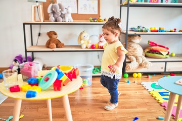 Beautiful toddler playing with building wooden blocks toys at kindergarten