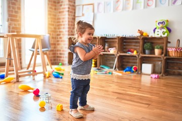 Beautiful toddler standing on the floor applauding and smiling at kindergarten