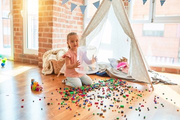 Beautiful blond toddler girl playing with constuction blocks outside tipi at kindergarten