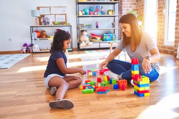 Beautiful teacher and toddler girl playing with construction blocks bulding tower at kindergarten