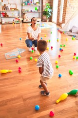 Fototapeta premium Beautiful teacher and toddler boy playing with colored small balls at kindergarten