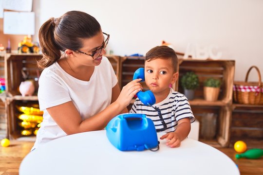 Beautiful teacher and toddler boy playing with vintage blue phone at kindergarten