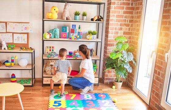 Beautiful teacher and toddler boy sitting on puzzle playing with numbers at kindergarten