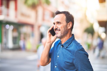 Middle age handsome businessman standing on the street talking on the smartphone smiling