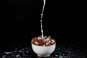 white bowl with assorted cereal with milk splashes isolated on black