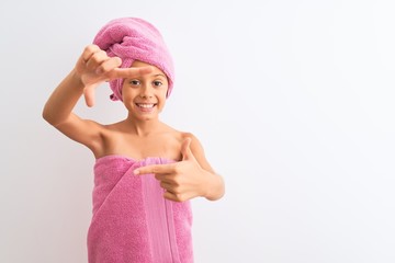 Beautiful child girl wearing shower towel after bath standing over isolated white background smiling making frame with hands and fingers with happy face. Creativity and photography concept.