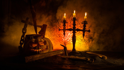 Scary orange pumpkin with carved eyes and a smile with burning candles and an ax
