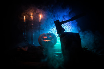 Scary orange pumpkin with carved eyes and a smile with burning candles and an ax