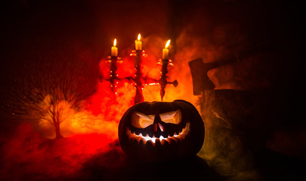 Scary orange pumpkin with carved eyes and a smile with burning candles and an ax - Powered by Adobe