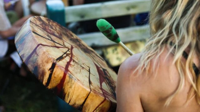 Sacred drums at spiritual singing group. A beautiful and colorful rawhide drum is seen in the hand of a young woman as people come together to experience shamanic powwow ceremony and culture.