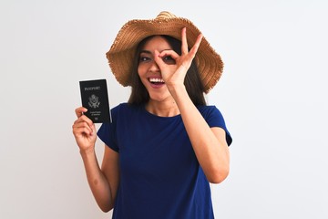 Beautiful tourist woman wearing hat holding USA passport over isolated white background with happy face smiling doing ok sign with hand on eye looking through fingers