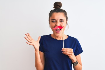 Young beautiful woman holding fanny party mustache over isolated white background very happy and excited, winner expression celebrating victory screaming with big smile and raised hands