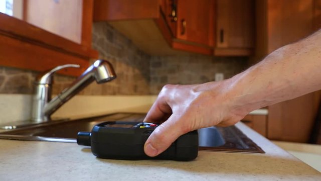Indoor damp & air quality (IAQ) testing. Closeup footage of a man using an electronic device to detect for signs of mold & harmful spores in a residential kitchen during an environmental quality test.