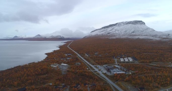 Kilpisjarvi village, Aerial, reverse, drone shot, overlooking the town, the e8 road and first snow on Saana tunturi mountain, on a cold, autumn morning, in Enontekio, Finland