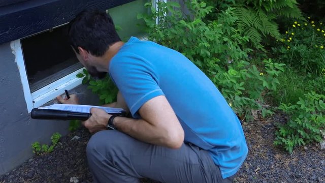 Indoor damp & air quality (IAQ) testing. A short movie shot in slow motion of a professional residential property surveyor at work, inspecting exterior walls and taking notes on paper and a clipboard.